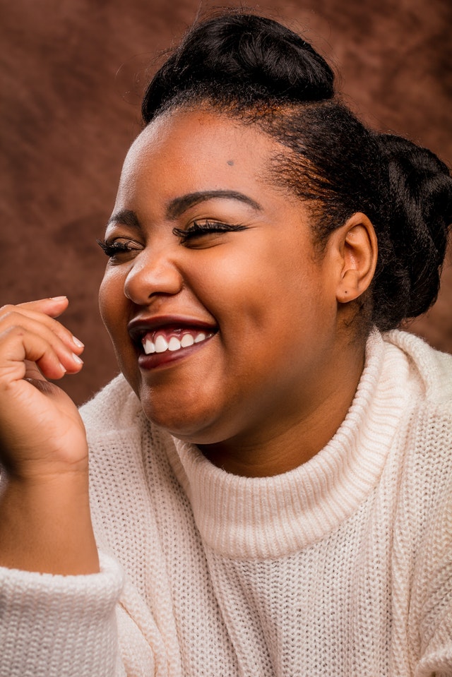 Black woman smiling in white sweater with brown background. #blacklivesmatter