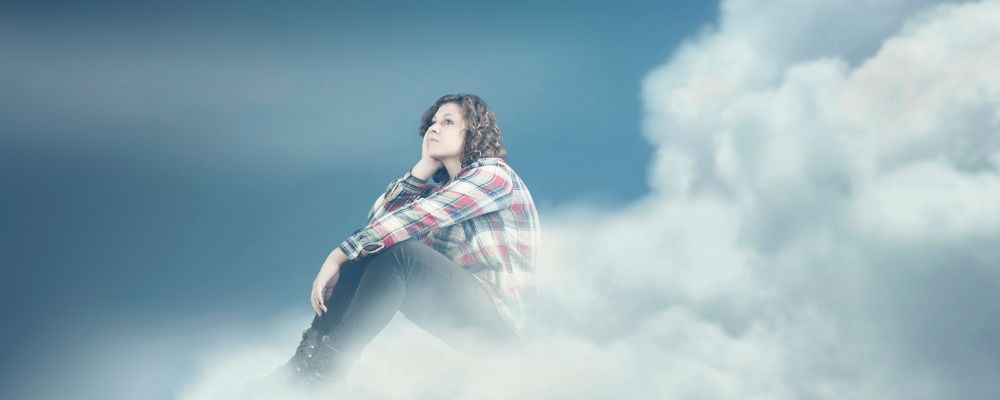 Dissociation, image of a woman sitting in clouds looking off into the distance